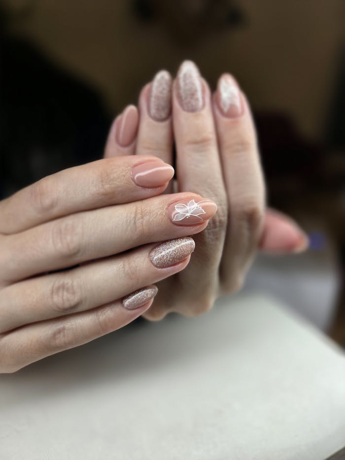 Close-up of elegant nude and glitter manicure with floral design on nails.